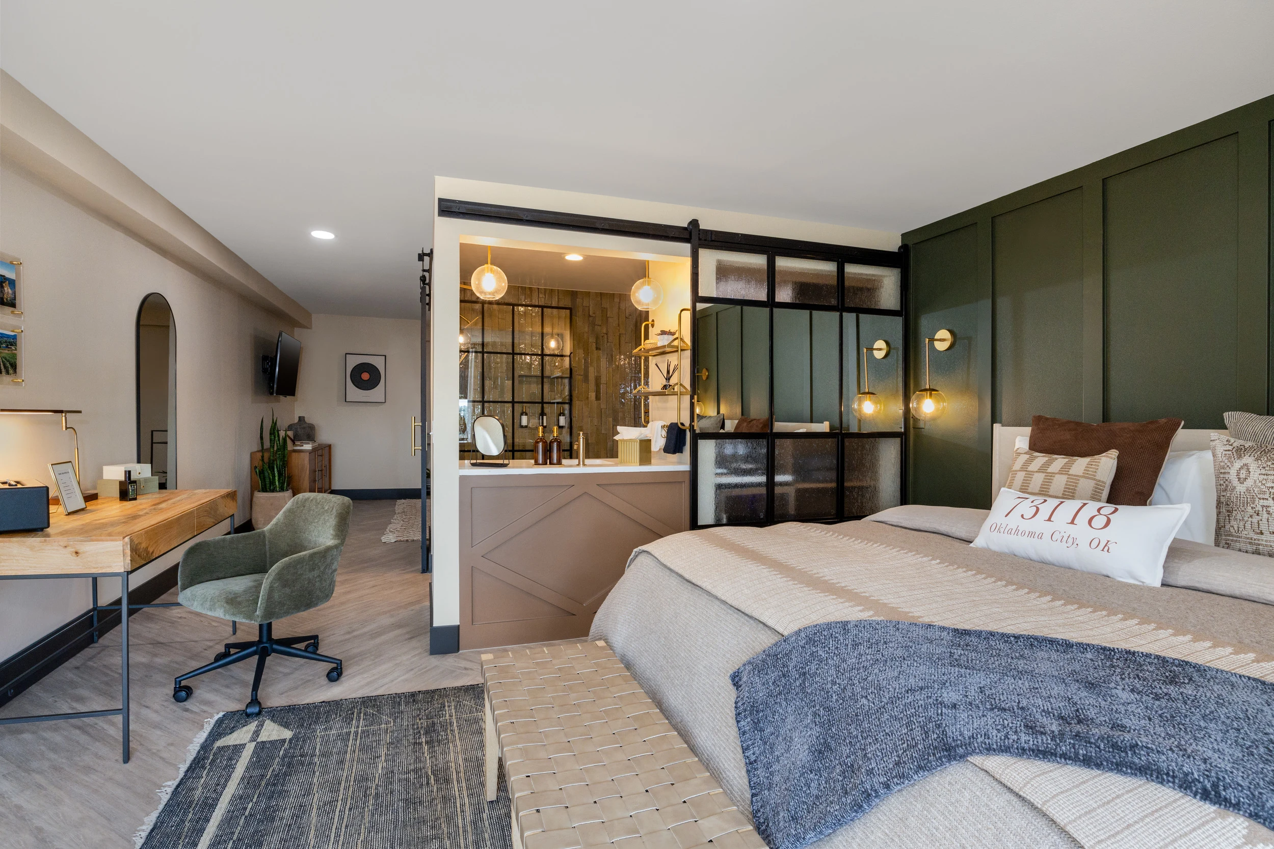 Modern hotel rooms in Oklahoma City feature a plush bed, wooden desk, and sleek glass partitions.