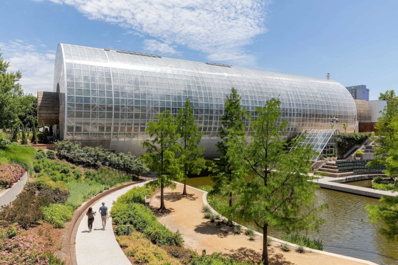 A modern glass conservatory sits beside a lush park path, offering fun things to do in Oklahoma City.