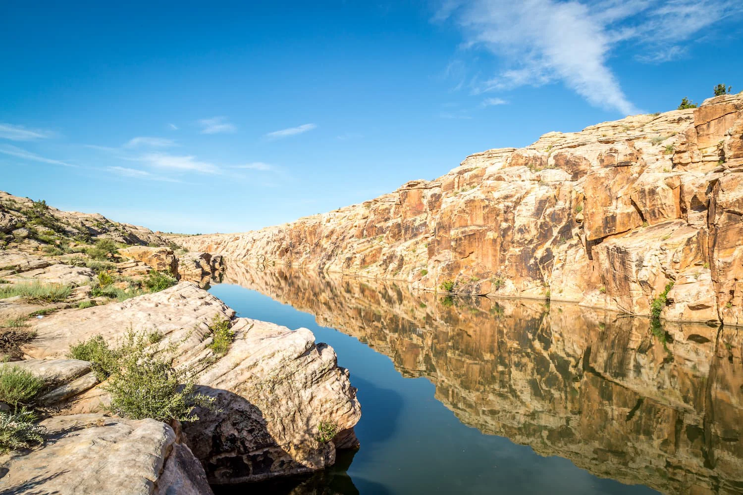 Rugged canyon with sandstone cliffs and a narrow, calm river flowing through it.