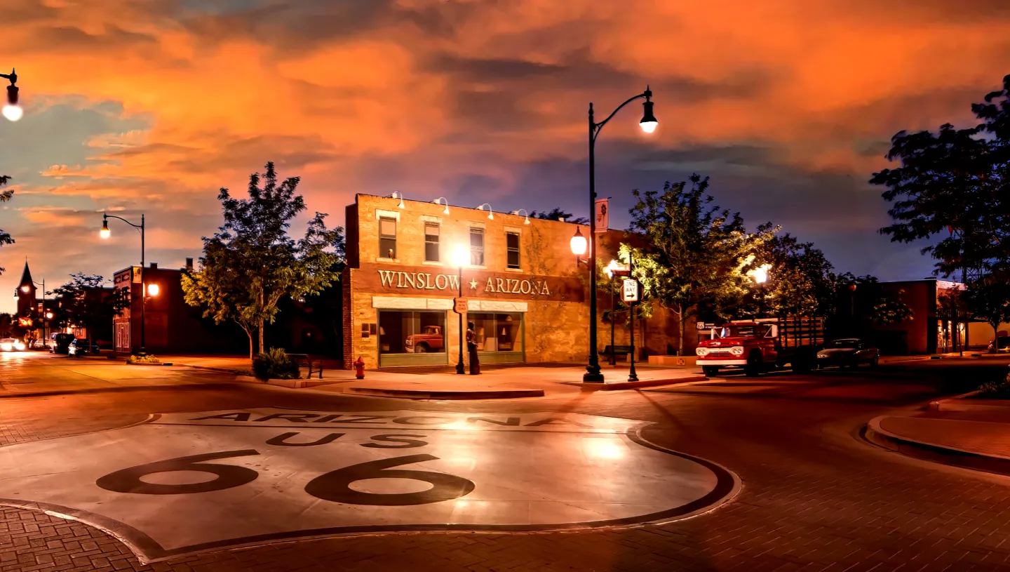 A nighttime scene of a street corner with a large "66" painted on the road, featuring a building with a sign reading "Winston Plaza" and a streetlight.