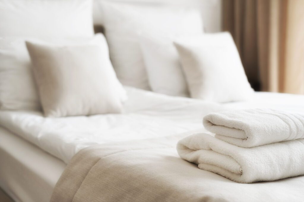 Selective focus on white fresh towels in hotel bed. Room service concept. Closeup white on new bedding and personal hygiene items.