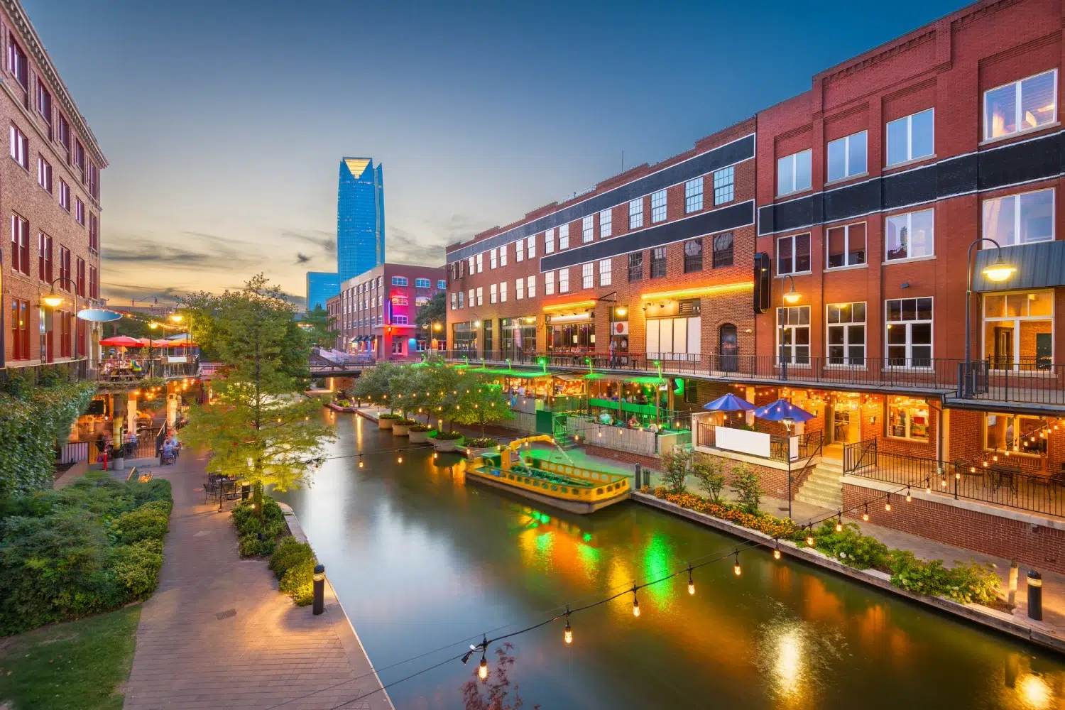 A canal with a brick building along it, featuring a boat, streetlights, and a sidewalk.