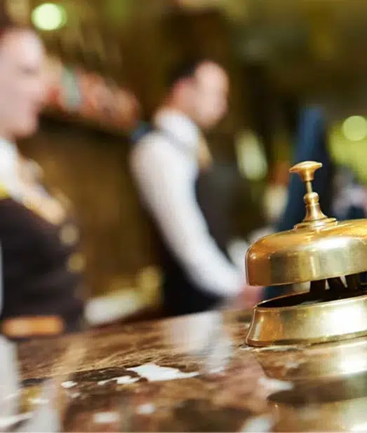 A brass bell on a marble countertop with a man in a white shirt and vest in the background.