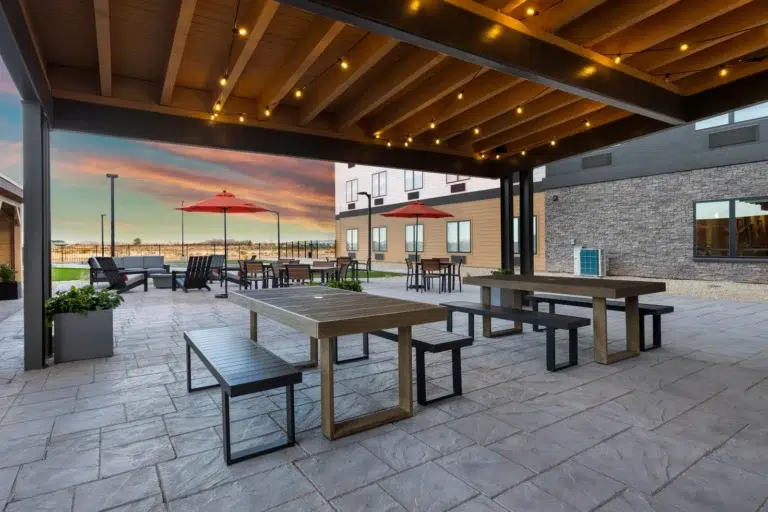 Outdoor seating area with tables and chairs, large stone patio, and a building in the background.