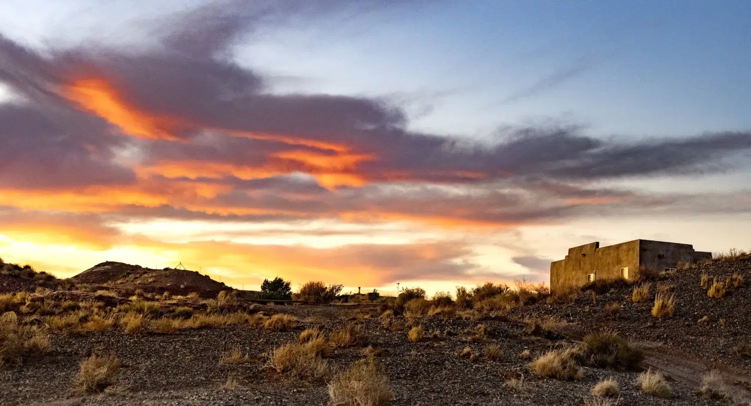 A desert landscape with a building in the distance, set against a vibrant sunset sky.